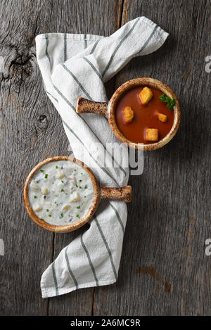 Flach mit zwei Schalen mit hausgemachten Clam Chowder und Tomaten Suppe auf einem rustikalen Holztisch mit einem Küchentuch. Stockfoto