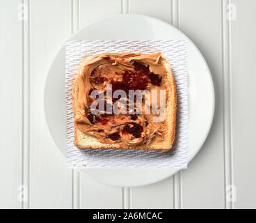 Overhead shot aus einer Scheibe Toast mit Erdnussbutter und Marmelade, auf einer Papierserviette und weiße Platte. Stockfoto