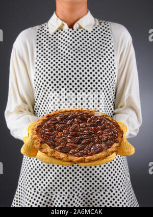 Nahaufnahme einer Hausfrau in einer Schürze und ofenhandschuhe Holding einen frisch gebackenen Urlaub Pecan Pie. Stockfoto