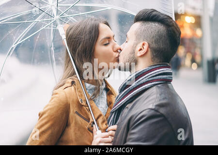Junges Paar Küssen unter dem Dach im regnerischen Tag im Stadtzentrum - romantischer Liebhaber ein bewegender Moment im Freien Stockfoto