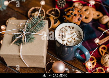 Becher mit heißem Kaffee, Geschenkverpackung mit Nadelbaum auf der Oberseite, Cookies und Girlande Stockfoto