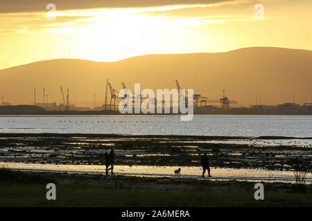 Belfast Lough, Holywood, County Down, Nordirland. Oktober 2019. Wetter in Großbritannien - ein heller, sonniger Tag mit klarem Himmel sah die Menschen an der Küste spazieren. Die Temperaturen fallen auf rund 4C über Nacht an Orten mit lokalen Bodenfrost Prognose Inland. Sonnenuntergang über dem Divis Mountain mit Belfast und Werftkranen im Vordergrund. Kredit: David Hunter/ Alamy Live Nachrichten. Stockfoto