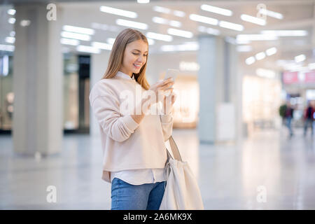 Ziemlich lässig Frau Scrollen in Smartphone auf der Suche nach on-line-Waren Stockfoto