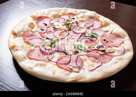 Billige Pizza mit Salami, Zwiebeln und Pilze. Stockfoto