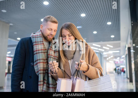 Junge lächelnde Frau ihren Ehemann, was Sie auf saisonale Verkauf gekauft angezeigt Stockfoto