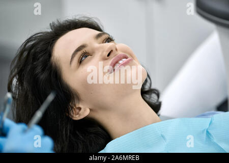 Schöne Mädchen in blauer Latzhose Patienten in einer Zahnarztpraxis. Zahnarzt in schützende Latex Handschuhe hält Instrumente. Closeup horizontale Foto. Stockfoto