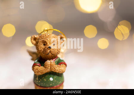 Dekorative Figuren aus einem Thema Weihnachten. Figurine eines süßen Bär mit Angel Wings. Festliches Dekor, warme Bokeh leuchtet. Stockfoto