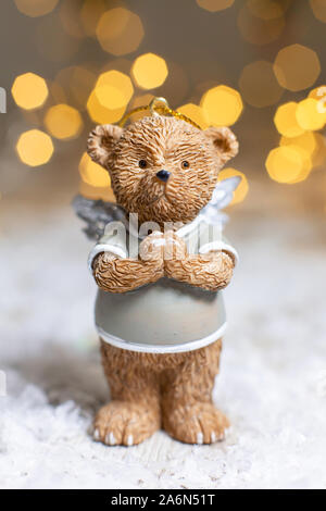 Dekorative Figuren aus einem Thema Weihnachten. Figurine eines süßen Bär mit Angel Wings. Festliches Dekor, warme Bokeh leuchtet. Stockfoto