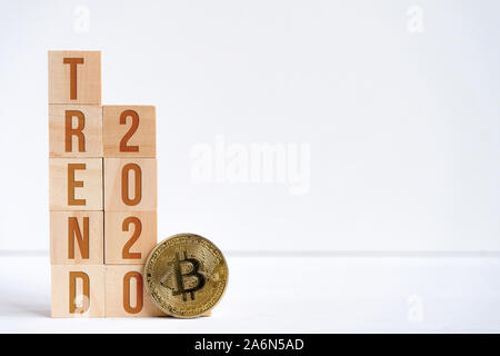 Ziffern 2020 und Wort Tendenz auf Holz Würfel neben Bitcoin. Das Konzept der hohen Nachfrage und der Erfolg der cryptocurrency im neuen Jahr. Kopieren Sie Platz. Stockfoto