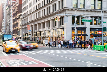 NEW YORK CITY 2019: Taxis und Menschen hetzen durch die Kreuzung der 23. Straße und 5th Avenue während einer anstrengenden Nachmittag rush hour Pendeln in Midtown Stockfoto