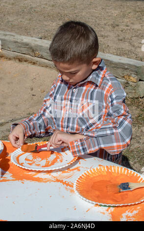 Ein junger spanischer Junge malt ein Papier der Platte an einen Herbst Jahrmarkt, eine hausgemachte Kürbis Deko für Halloween Stockfoto