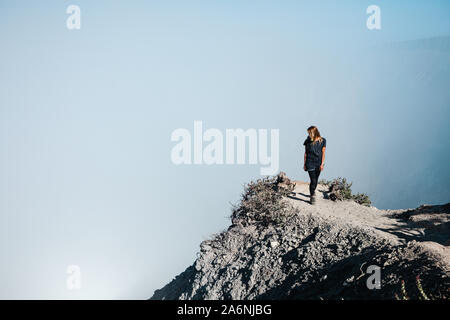 Junge Frau in Schutzmaske auf dem Gipfel des aktiven Vulkan Kawah Ijen Krater oben Säure See mit giftigen Dämpfe. Beliebtes Reiseziel. Stockfoto