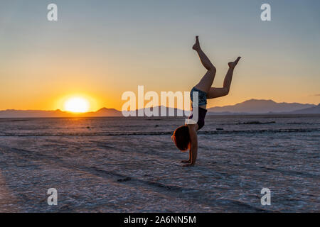 Schöne Frau macht Handstand während des Sonnenuntergangs in Bonneville Salt Flats Stockfoto