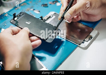 Nahaufnahme der Handwerker mit tweezzers broker Mikrofon des Smartphones zu entfernen. Stockfoto