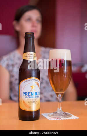 Sapporo Premium alkoholfreies Bier im Glas mit unscharfen schönen kaukasischen Frauen im Hintergrund Stockfoto