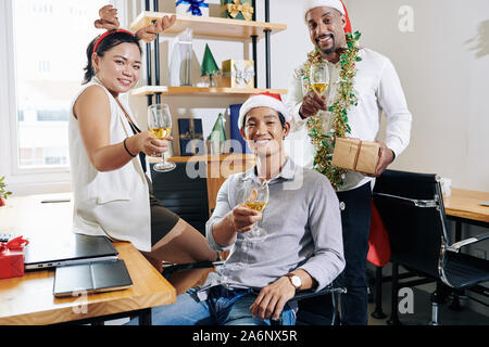 Multi-ethnischen Business Team tragen Nikolausmützen und Rentier Geweih, wenn geniessen Weihnachtsfeier bei Small Office Stockfoto