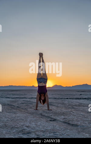 Schöne Frau macht Handstand während des Sonnenuntergangs in Bonneville Salt Flats Stockfoto