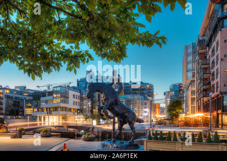 Oslo, Norwegen - 24. Juni 2019: Nacht Blick auf Pferd Statue auf der Straße und Wohngebiet mehrstöckige Häuser im Viertel Aker Brygge. Sommerabend. Fa Stockfoto