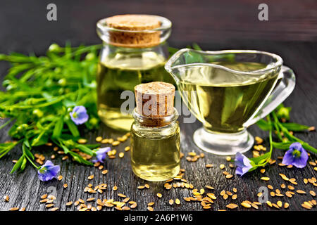 Leinöl in zwei Gläser und eine Sauciere mit Samen, Blätter und Blüten von Flachs auf dunklen Holzplatte Hintergrund Stockfoto