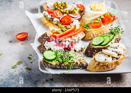 Toast mit verschiedenen Belägen auf grau-braunen Hintergrund, Kopieren offenen Raum. Crostini mit Banane und Erdnussbutter, Pastete, Avocado, Lachs, Ei, Käse Stockfoto