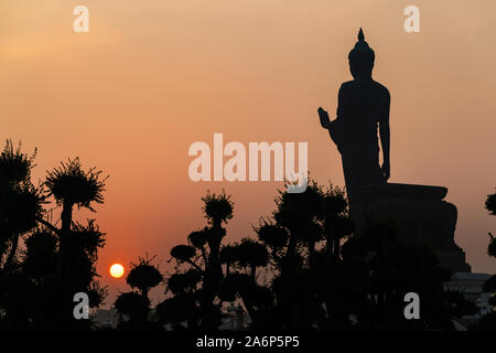 Silhouette Stehender Buddha Statue in Abhaya mudra Pose und linke Hand heben mit Sonne auf der entgegengesetzten Seite Stockfoto