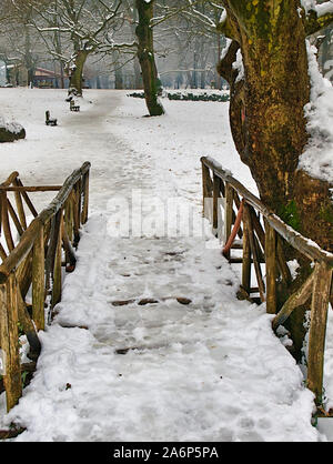 Eis überdachte Holzbrücke weg und Bänke im Schnee Agios Nikolaos (Sankt Nikolaus) Park in Syros Griechenland. Stockfoto