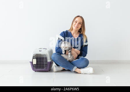 Charmante positive junge Frau hält in ihrer Hände ihre schönen grauen schottischen Katze sitzt auf dem Boden in eine neue Wohnung. Pet-Konzept. Stockfoto