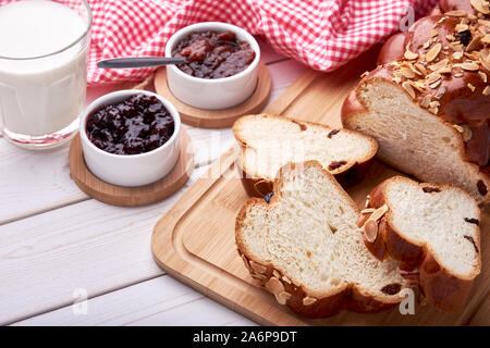 Stillleben mit gestrickten Weihnachten Kuchen und süßes Gebäck mit Rosinen und Mandeln. Auf weißem Holzbrett Tabelle mit Schüsseln mit Marmelade in Scheiben geschnitten, Glas o Stockfoto