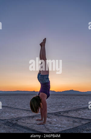 Schöne Frau macht Handstand während des Sonnenuntergangs in Bonneville Salt Flats Stockfoto