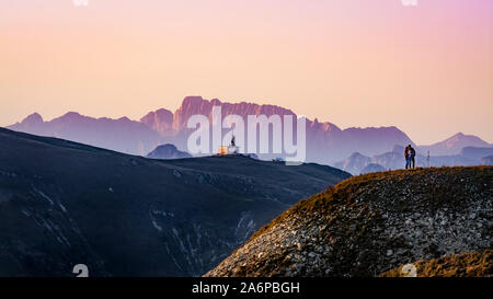 Ein paar Leute stehen auf dem Gipfel des Mount Pizzoc (Venetien, Italien) bei Sonnenuntergang im Herbst. Alpen und Dolomiten im Hintergrund Stockfoto