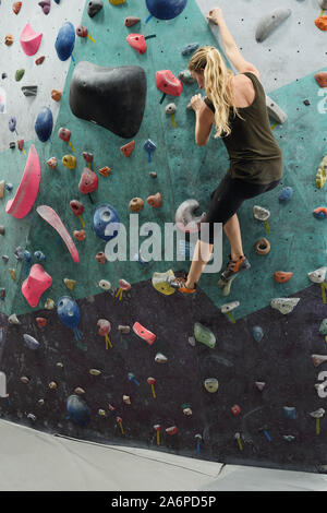 Junge aktive weibliche Holding durch künstliche Felsen an der Wand beim Klettern Praxis Stockfoto