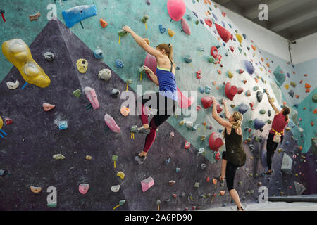 Gruppe von drei jungen Sportler in activewear Ausübung auf Kletterwand Stockfoto