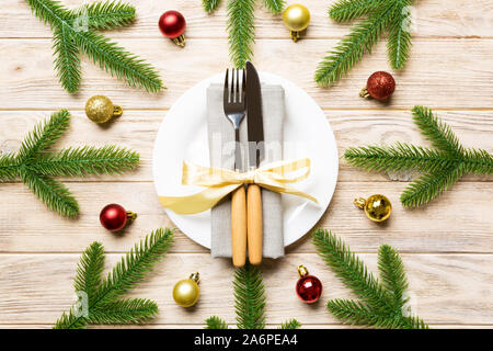 Blick von oben auf das neue Jahr Abendessen auf festliche Holz- Hintergrund. Zusammensetzung der Teller, Gabel, Messer, Tannenbaum und Dekorationen. Frohe Weihnachten Konzept. Stockfoto