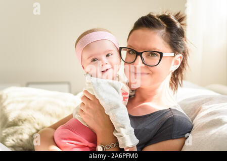 Mutter Holding schöne Happy Baby Mädchen in helle, sonnige Zimmer. Mutterschaft Konzept Stockfoto