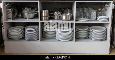 Stapel sauberen, weißen Platten und andere Metallgegenstände auf die Regale in kommerziellen Restaurant. Kommerzielle Geschirr sauber und ordentlich Stockfoto