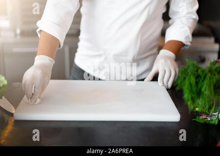 Nicht erkennbare Junge afrikanische Koch in professionellen Küche im Restaurant eine Mahlzeit Reinigung weiße plastiс Schneidebrett Stockfoto