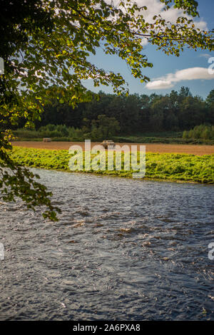 Landwirtschaftlichen Hintergrund der Heuballen aus gesehen über einen Fluss in einer wunderschönen Landschaft. Stockfoto