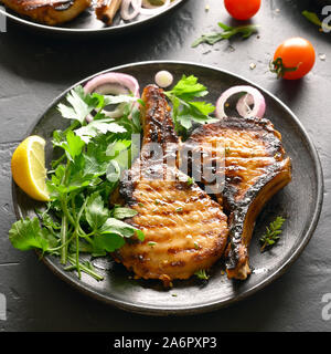 Gegrilltes Schweinefleisch Steaks mit pflanzliche Blätter auf die Platte über der schwarzen Steintisch. Nähe zu sehen. Stockfoto