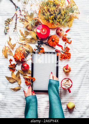 Weibliche Hände mit leeren Brief Board auf weiße Decke Hintergrund mit gelben Herbst Zweige und Blätter, brennende Kerzen, Kürbisse, rote Tasse cappuc Stockfoto