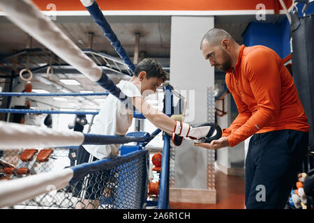 Professionelle talentierte Trainer erteilen Anweisungen an die kleinen Boxer. close up Side View Photo. Lehrer wünscht viel Glück zu seinem Schüler. Trainer unterstützt h Stockfoto