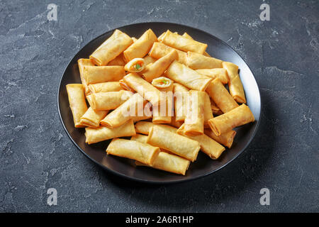 Frittierte knusprige Mundgerechte chinesische Frühlingsrollen mit Kohl, Möhren und Erbsen Füllungen auf eine schwarze Platte auf einer konkreten Tabelle, Ansicht von oben Stockfoto