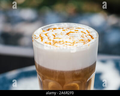 Hot Latte macchiato Kaffee mit Karamell auf der Tischplatte im Freien. Natürliche harte Tageslicht. Soft Focus mit Bokeh. Nähe zu sehen. Stockfoto