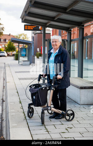 Über 90 Jahre alten aktiven älteren Dame warten auf den Bus an der Haltestelle allein, mit Gehhilfe Stockfoto