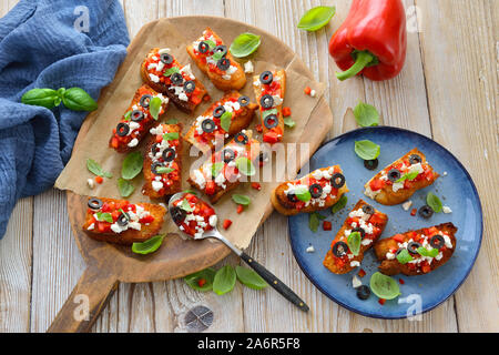 Warme Griechische bruschetta: knusprig gebackene kleine Scheiben Fladenbrot mit Feta Käse, schwarze Oliven, Paprika und Basilikum, als Vorspeise serviert. Stockfoto