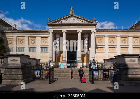 Ein Mädchen mit einem hellen roten Rollenkoffer Spaziergänge in Richtung am Eingang Ashmolean Museum, Oxford auf Beaumont Street im hellen Sonnenschein u Stockfoto