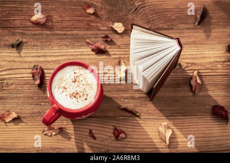 Kaffeetasse und offenes Buch auf Holztisch mit Blätter im Herbst. Ansicht von oben. Konzept der romantische Stimmung, zurück zur Schule, Bildung Stockfoto