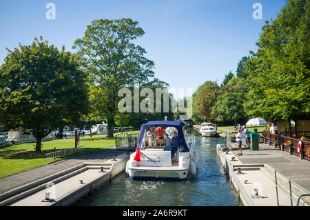 Ein kajütboot oder Boot verlässt den Tempel auf der Themse zwischen Marlow und Henley-on-Thames, im hellen Sonnenschein unter einem hellen klaren Blu Stockfoto