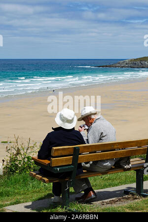 Elderley Rentnerehepaar auf einer Bank mit Blick auf den Fistral Beach in Newquay, Cornwall, England. Stockfoto