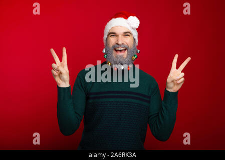 Glückliche junge bärtige Mann in weihnachtliche Stimmung mit Frieden Geste Stockfoto