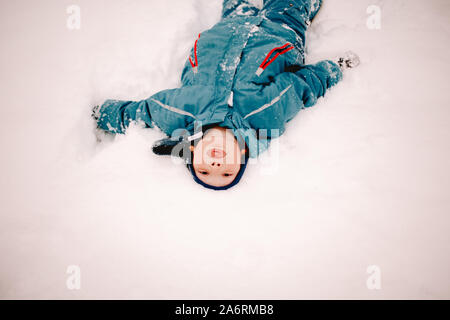 Verspielte Junge heraus haften Zunge, während im Schnee im Winter liegen Stockfoto